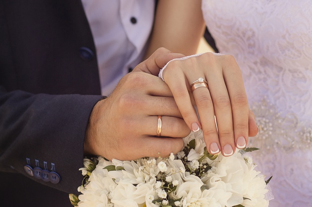 closeup-shot-newlyweds-holding-hands-showing-wedding-rings_181624-15865